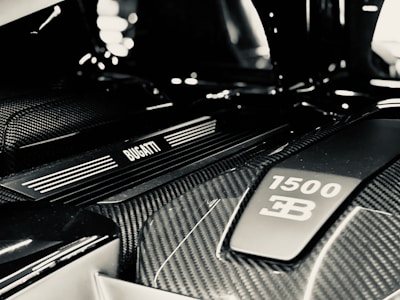 A detailed view of a car engine bay featuring a Bugatti emblem and a label indicating 1500 horsepower. The image highlights the sleek, modern design with prominent carbon fiber elements.