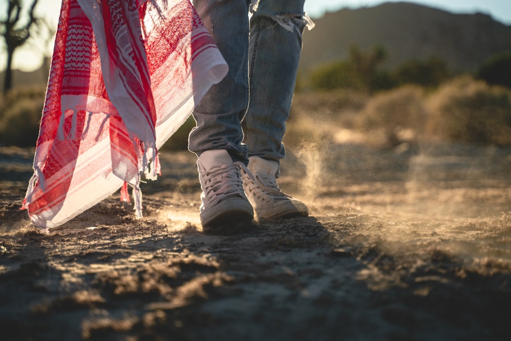 Person in blauen Jeans und schwarzen Stiefeln, die tagsüber auf braunem Sand steht