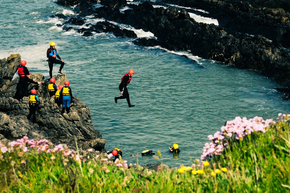 people in red jacket and black pants standing on rock near body of water during daytime