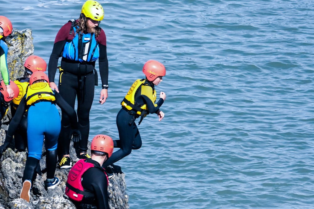 people in black and yellow wet suit wearing red helmet on black rock near body of with with with with