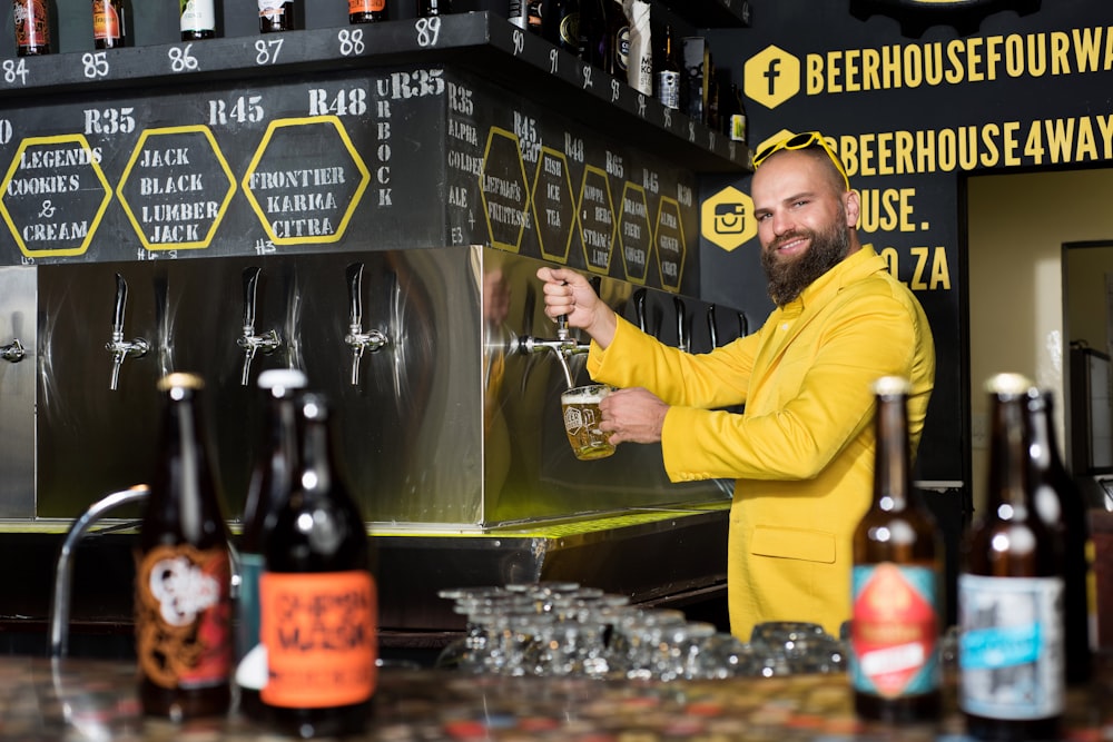 homme en chemise à manches longues jaune versant de l’alcool sur une bouteille en verre transparent