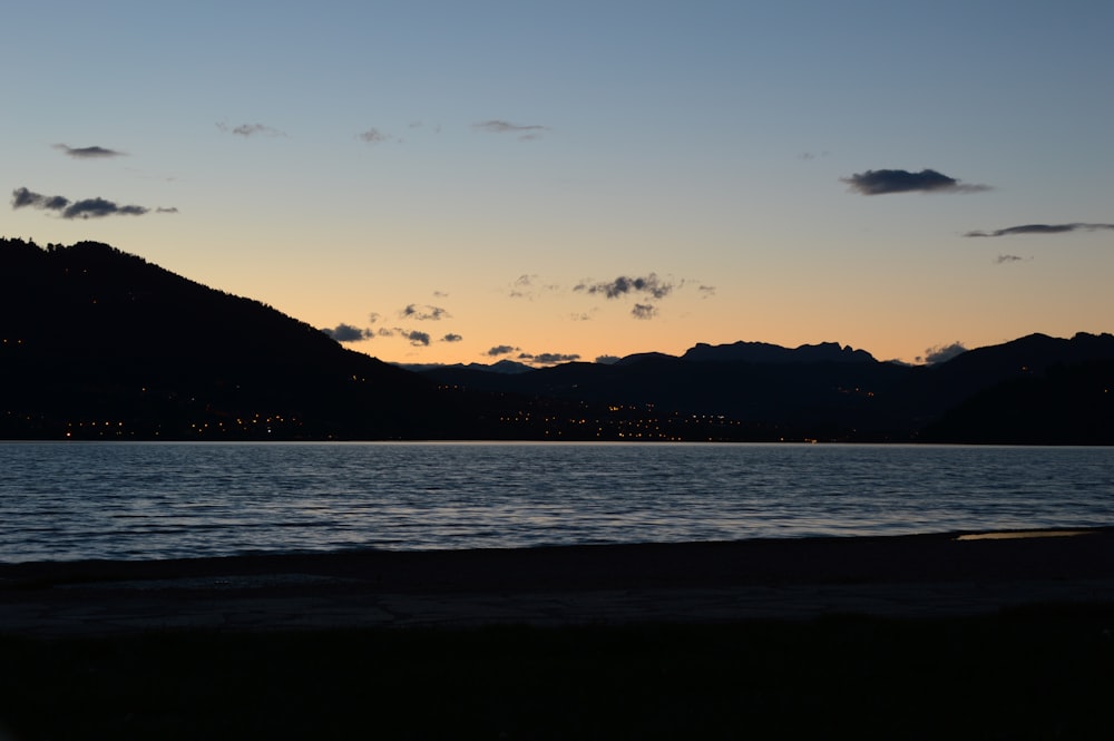 silhouette of mountain near body of water during sunset