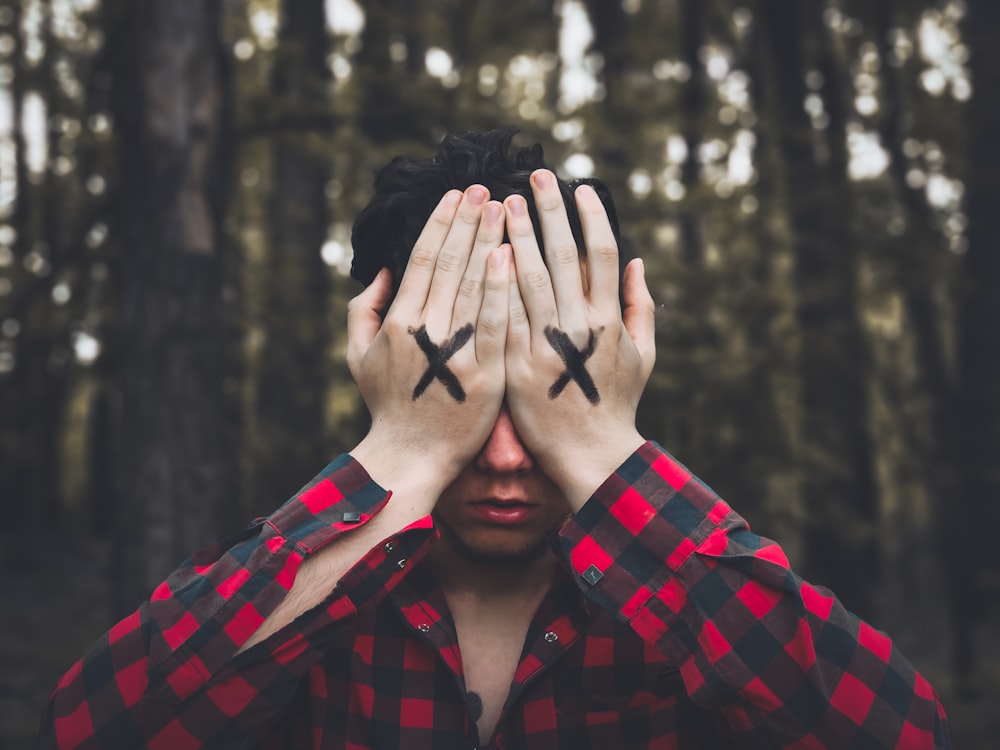 man in red and black plaid dress shirt covering face with hands