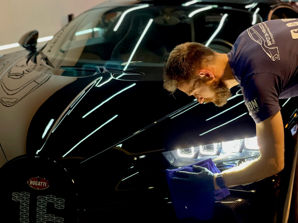 homem na camiseta azul do pescoço da tripulação em pé ao lado do carro preto