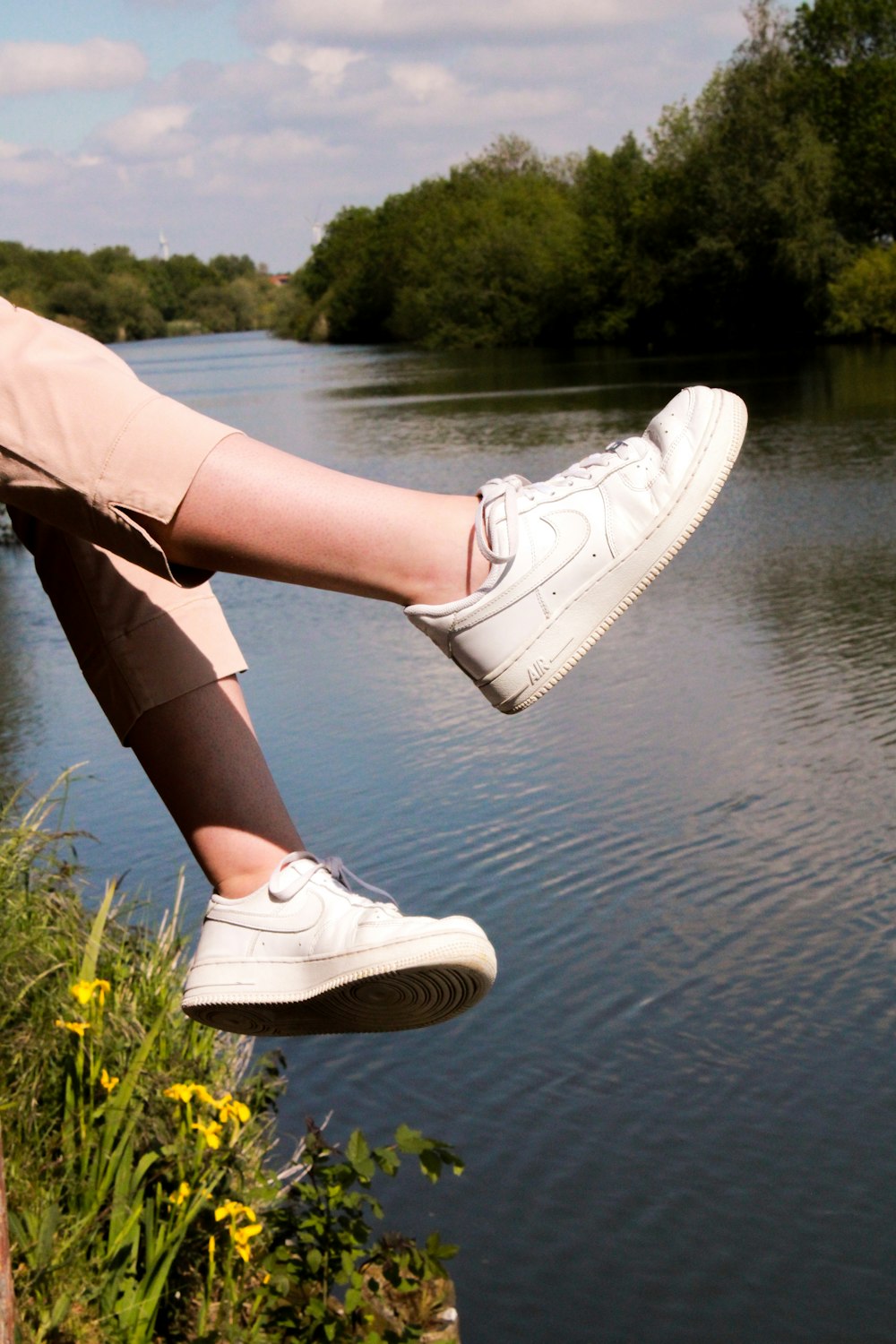 woman in white leather shoes standing on green grass near body of water during daytime