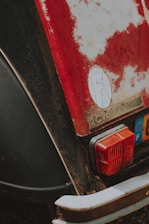 The image displays the rear section of a vintage car with visible wear and rust. The paint is chipped, revealing rusted metal underneath, and the model is identified as a 2CV6. A tail light and a European license plate are also visible.