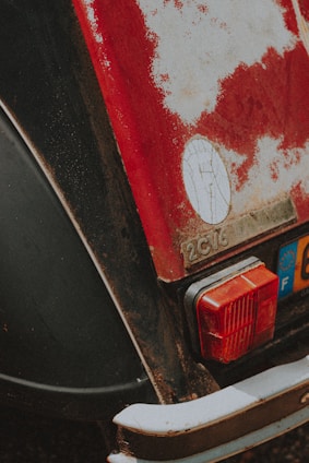 The image displays the rear section of a vintage car with visible wear and rust. The paint is chipped, revealing rusted metal underneath, and the model is identified as a 2CV6. A tail light and a European license plate are also visible.