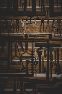 A collection of vintage tools is neatly arranged on a wooden backdrop, creating a rustic and historical atmosphere. The tools include various pliers, wrenches, and other woodworking equipment, showcasing aged and worn metal surfaces.