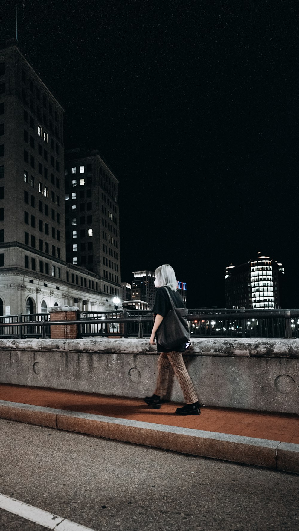 Mujer en vestido negro de pie en el puente de hormigón marrón durante la noche