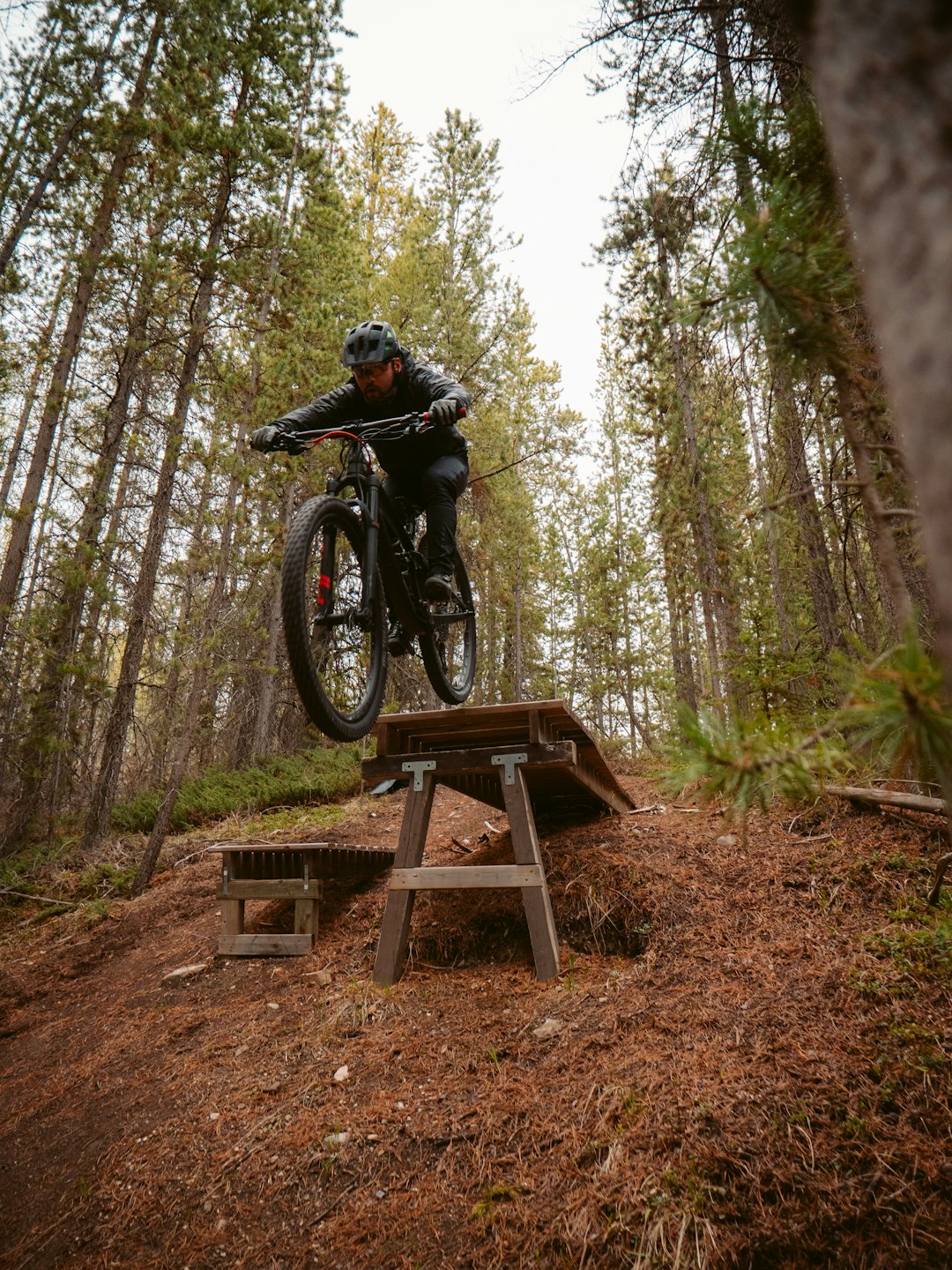 man riding black mountain bike on brown wooden table surrounded by trees during daytime