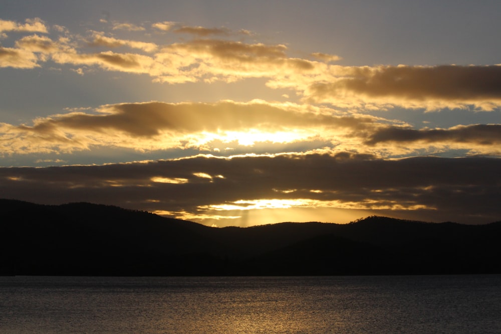 silhouette of mountain near body of water during sunset