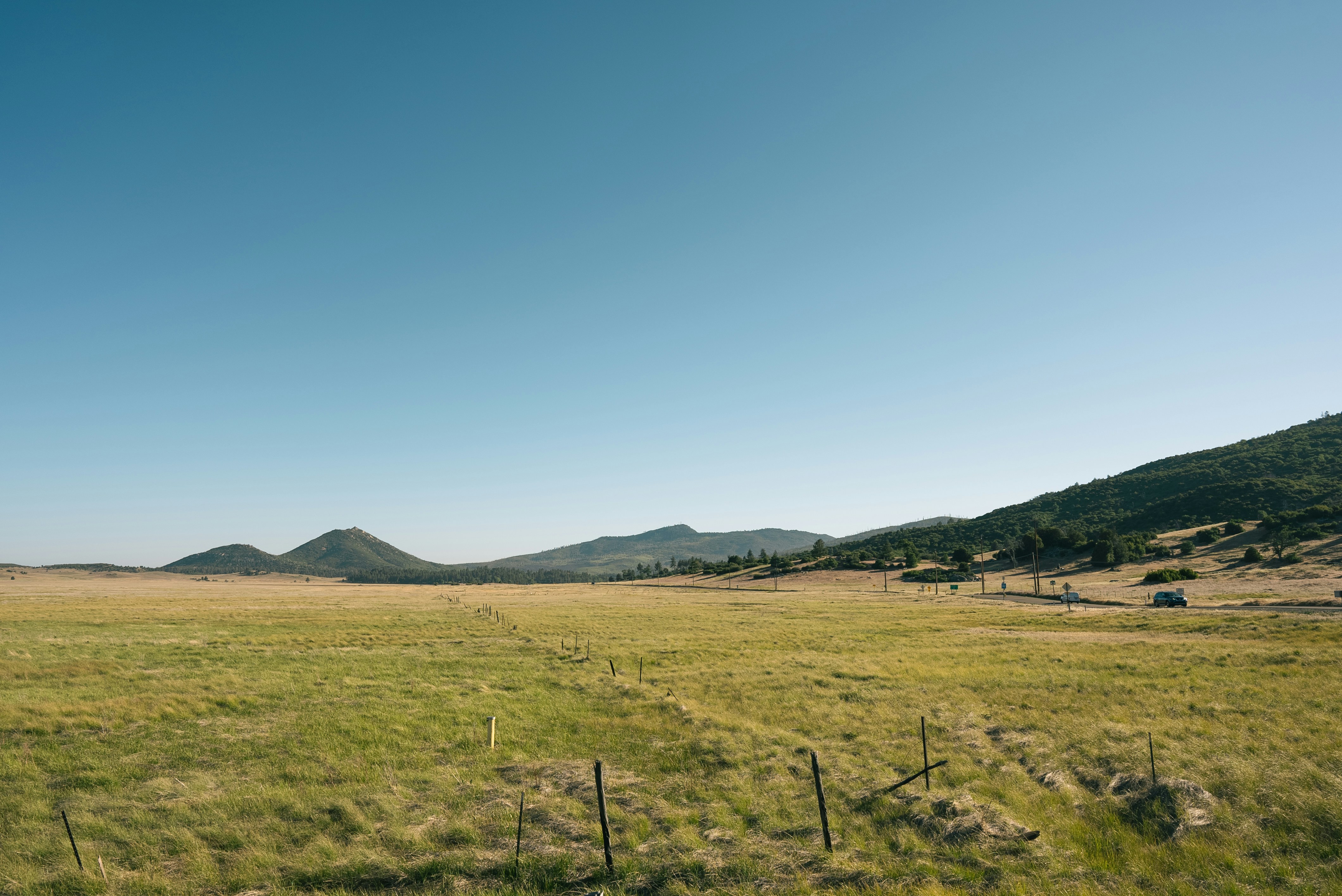 green grass field near mountain under blue sky during daytime
