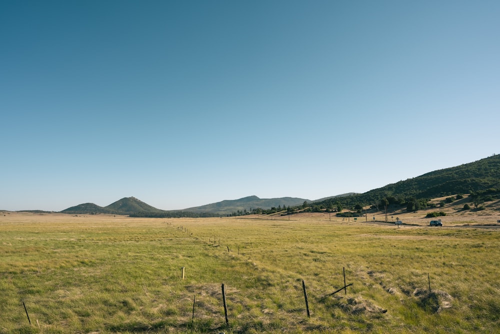 green grass field near mountain under blue sky during daytime