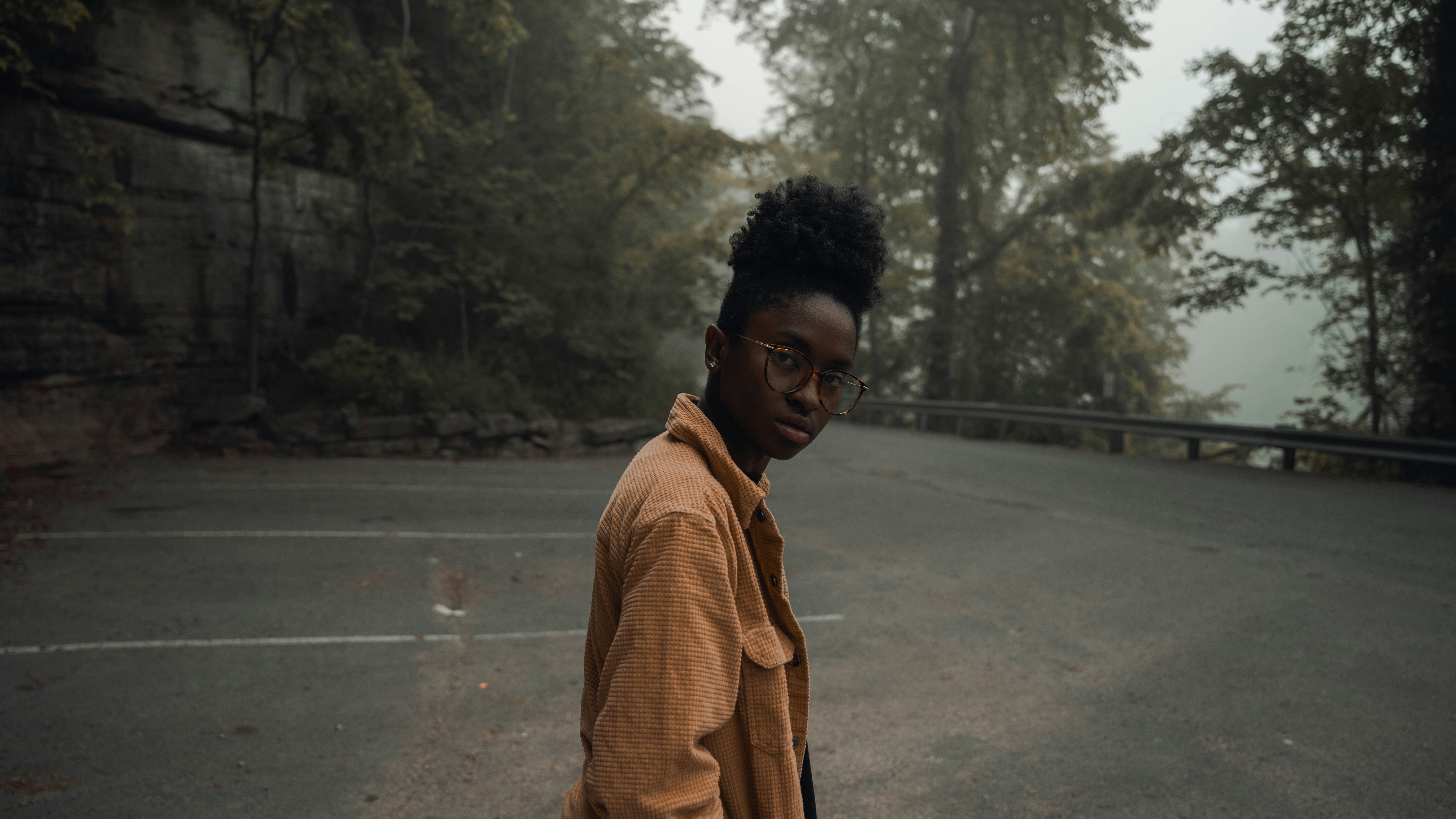 homem em casaco marrom em pé na estrada de concreto cinza durante o dia