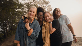 Four women laughing together in a line outdoors during the golden hour