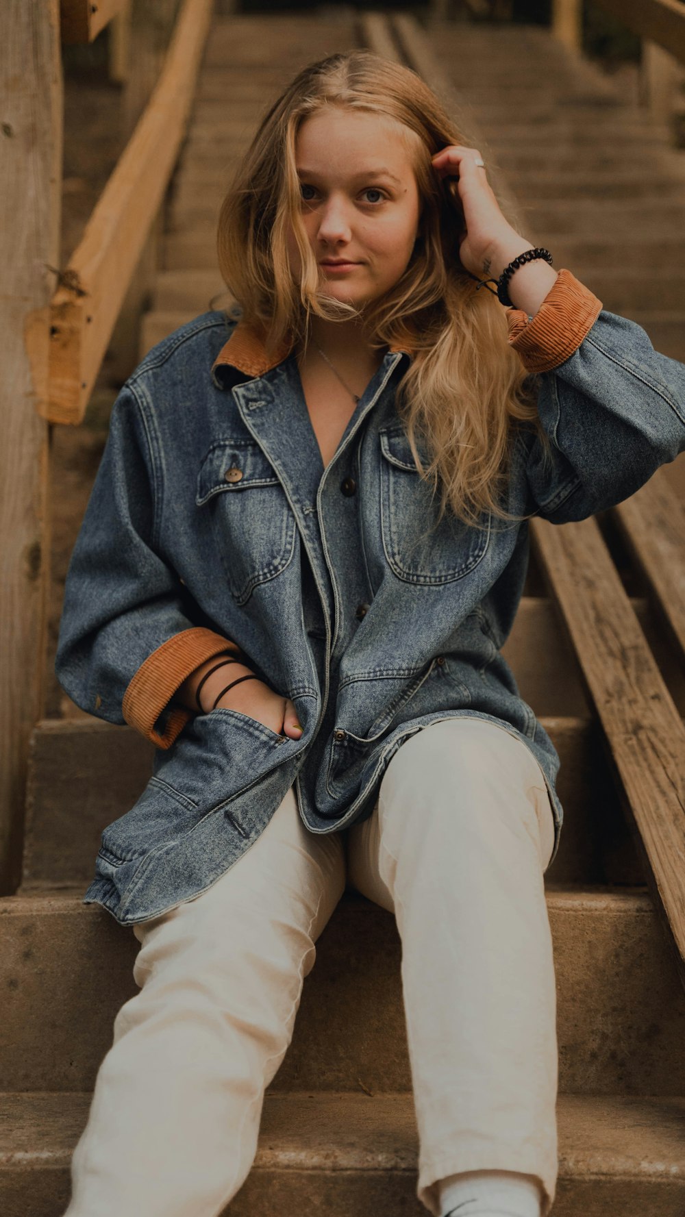 woman in blue denim jacket and white pants sitting on brown wooden bench