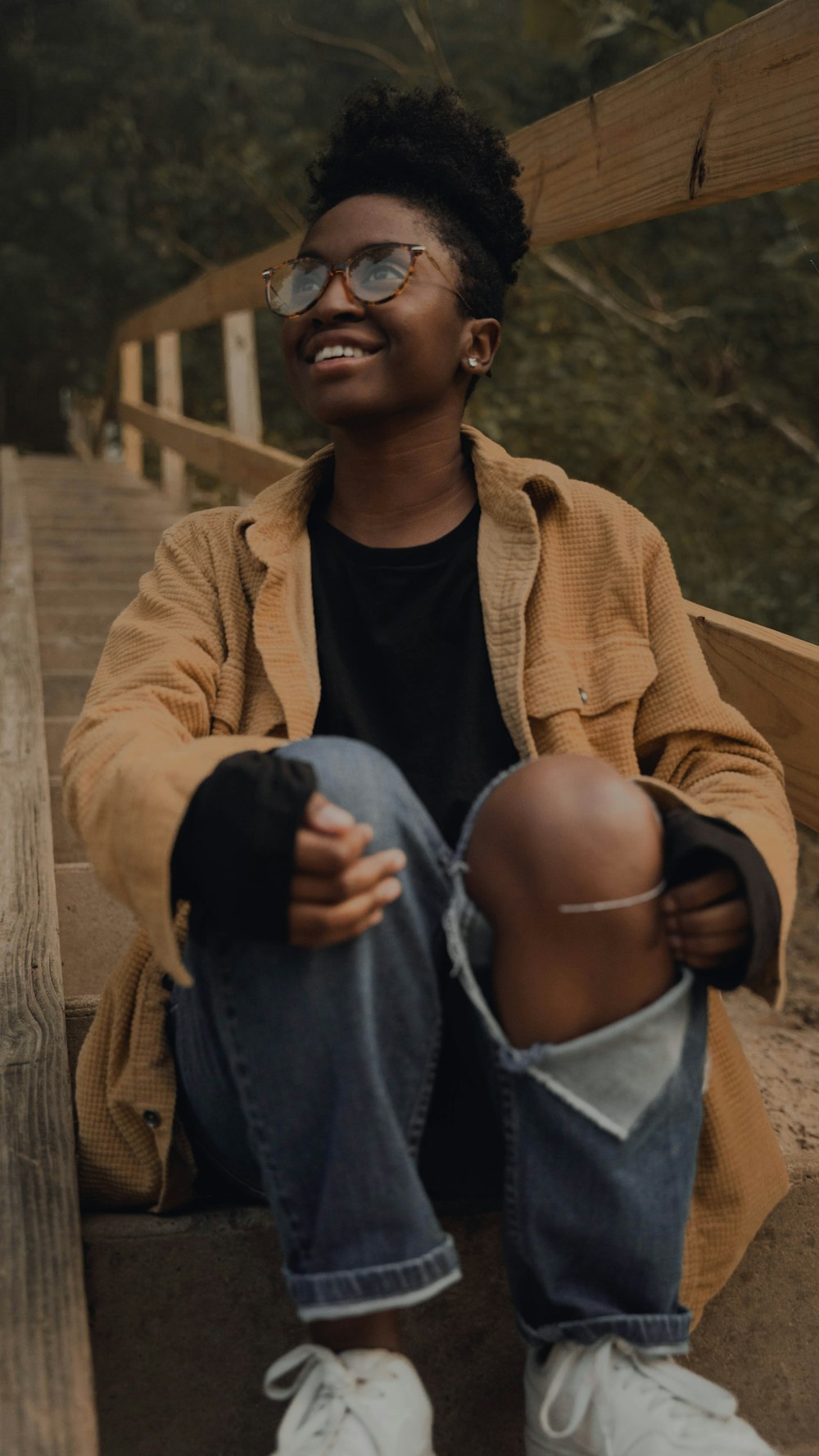 man in brown coat and blue denim jeans sitting on brown wooden stairs