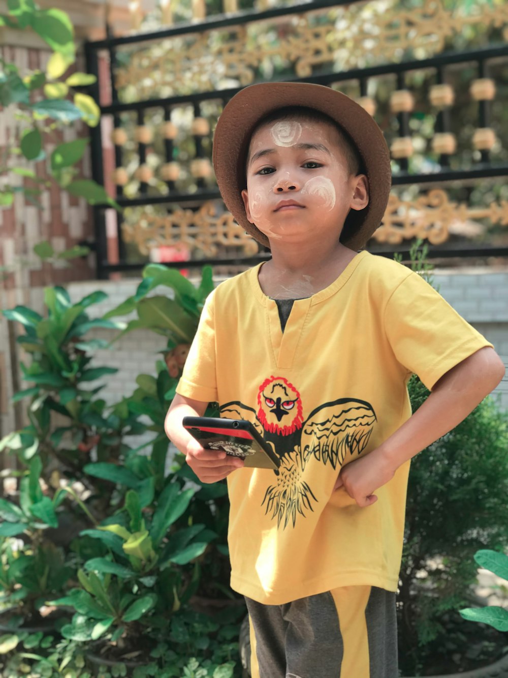 boy in yellow crew neck t-shirt wearing brown hat holding black smartphone