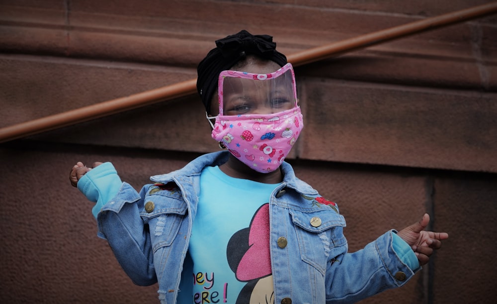 child in blue denim jacket wearing pink mask