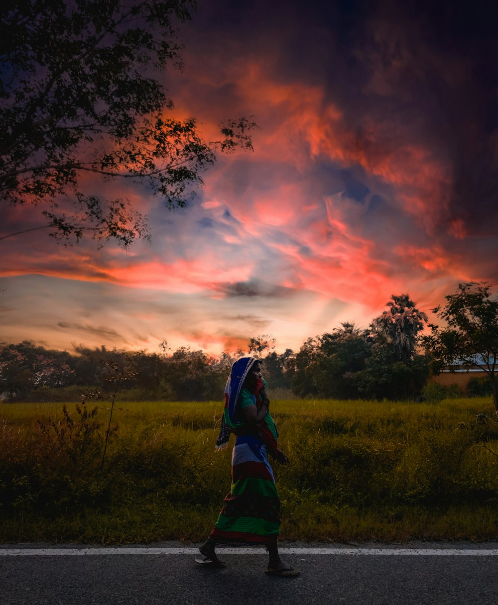 mulher no vestido azul e preto em pé no campo verde da grama durante o pôr do sol