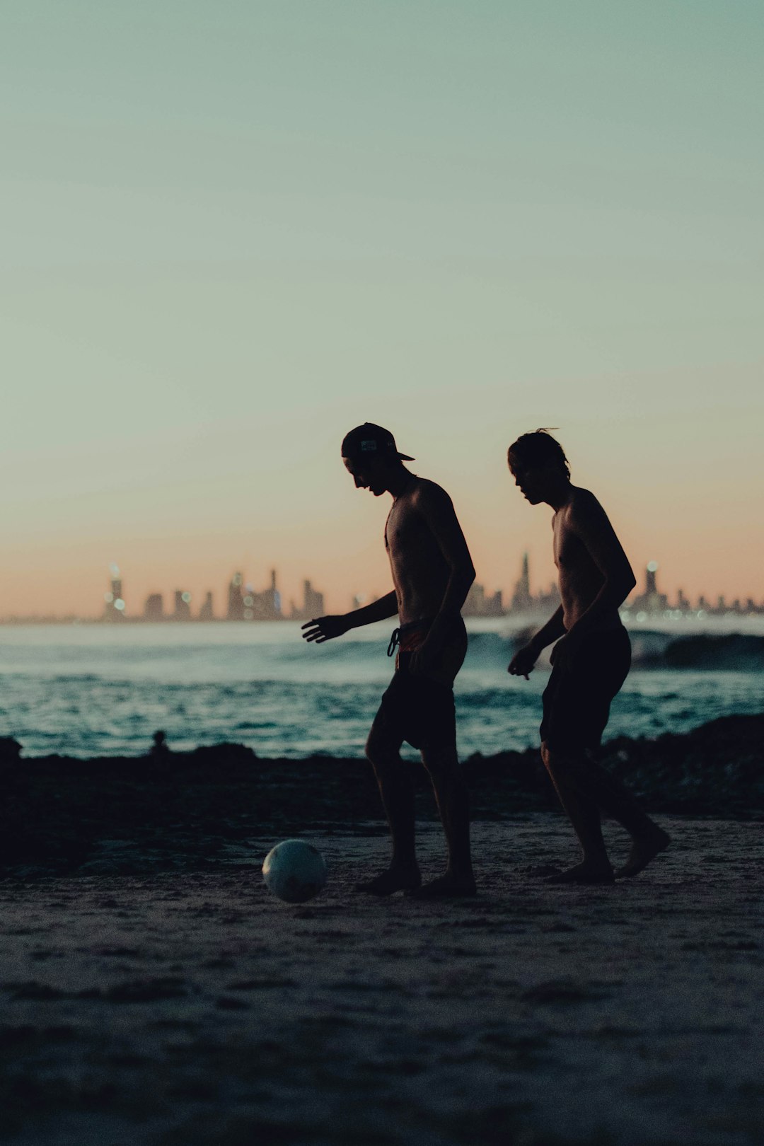 2 men playing soccer on beach during sunset