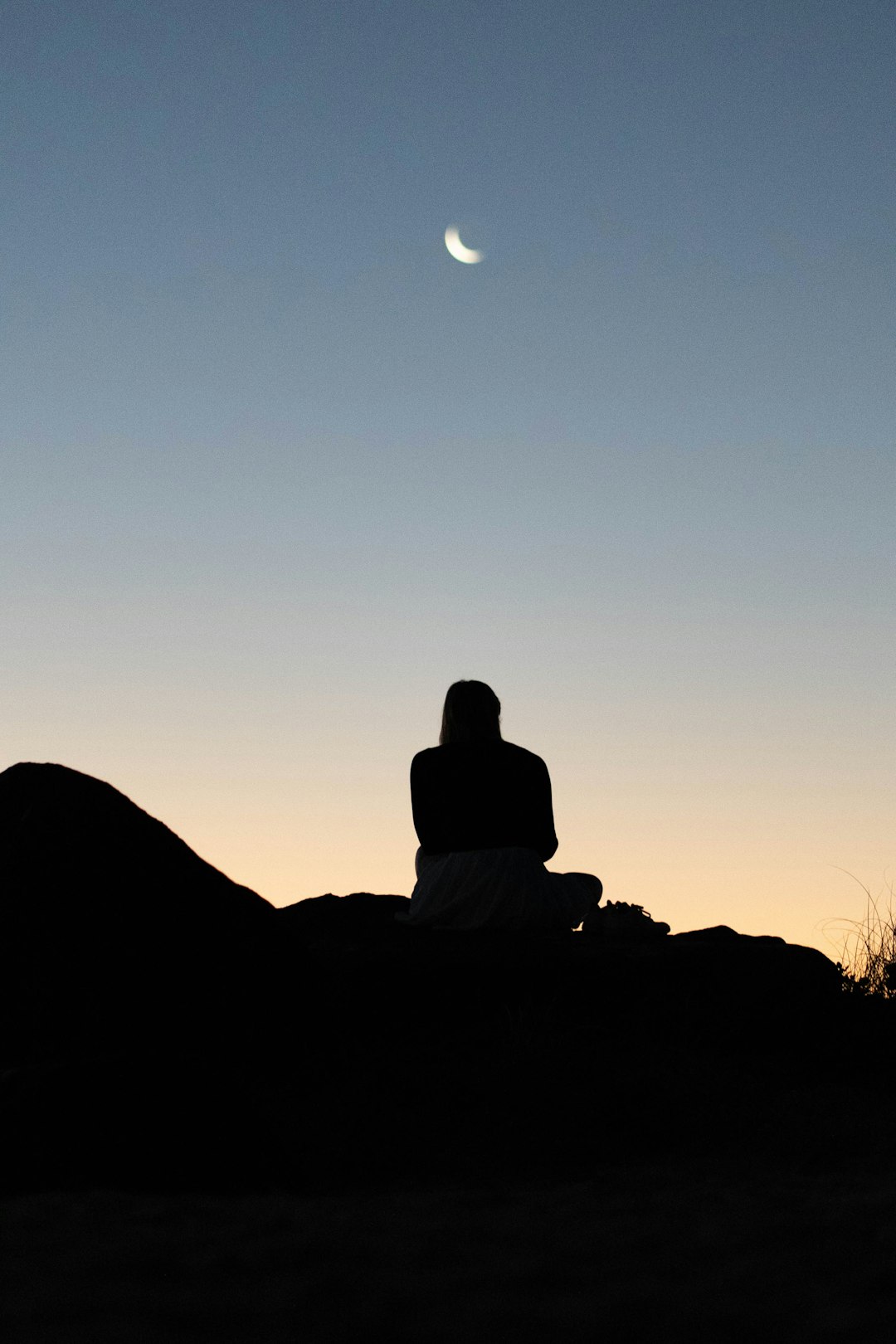 silhouette of person sitting on rock during sunset