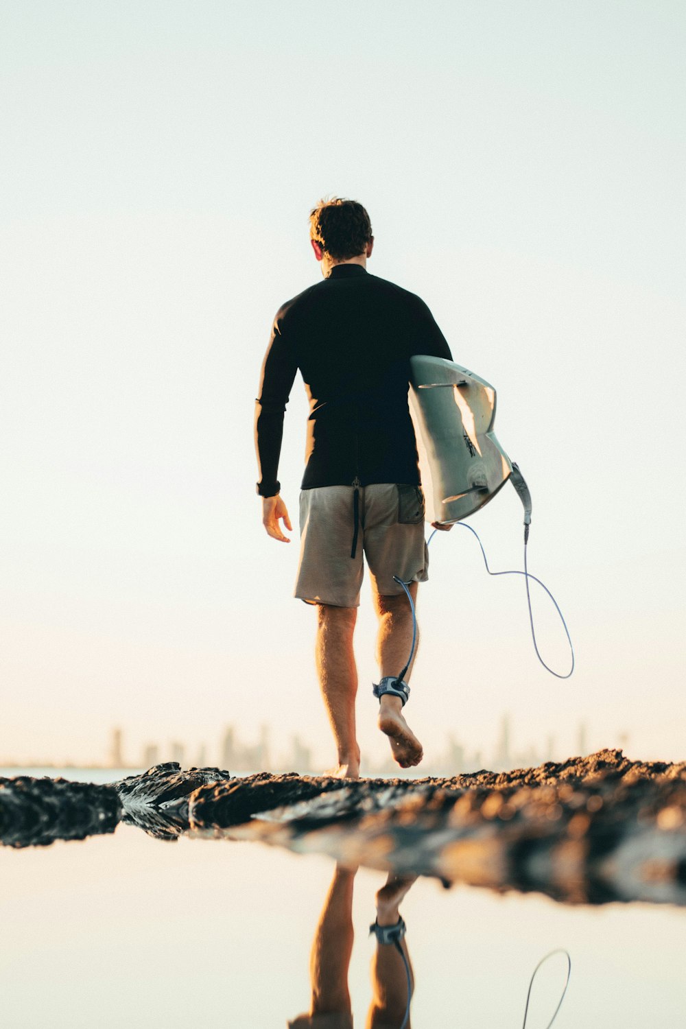 man in black long sleeve shirt and gray shorts carrying white and black surfboard during daytime