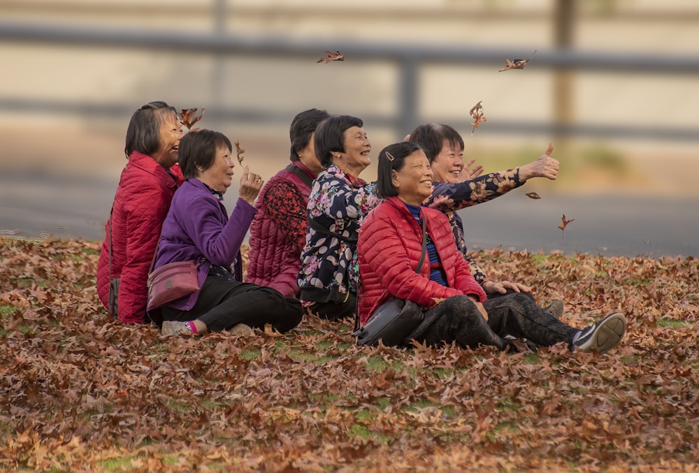 children sitting on dried leaves on ground during daytime