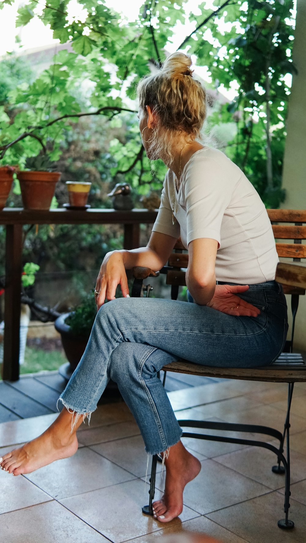 woman in white t-shirt and blue denim jeans sitting on brown wooden bench during daytime