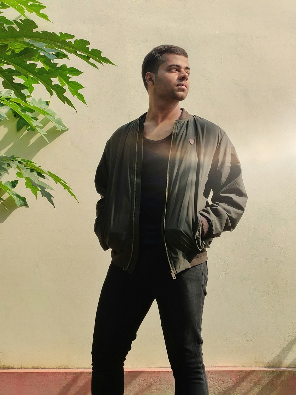 man in black leather jacket standing beside green plant