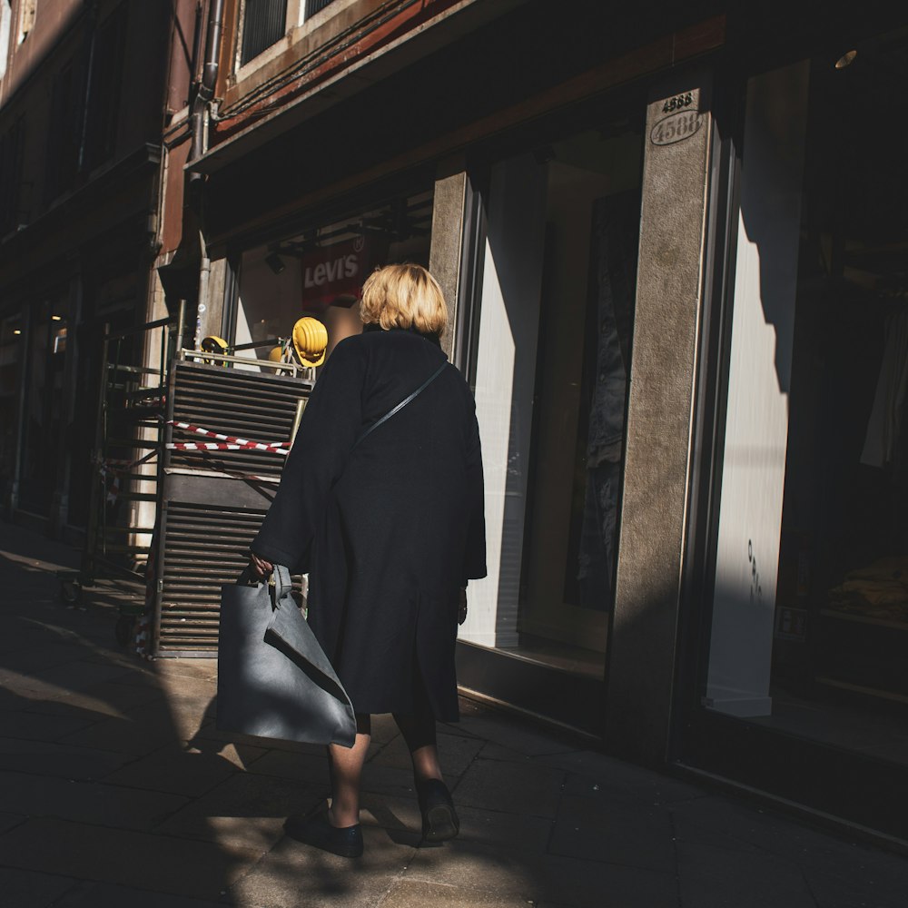 woman in black coat standing beside glass window during daytime