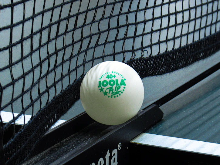 Close-up of the netzkraft training tool showing the flexible band and telescopic poles in use on a table tennis net.