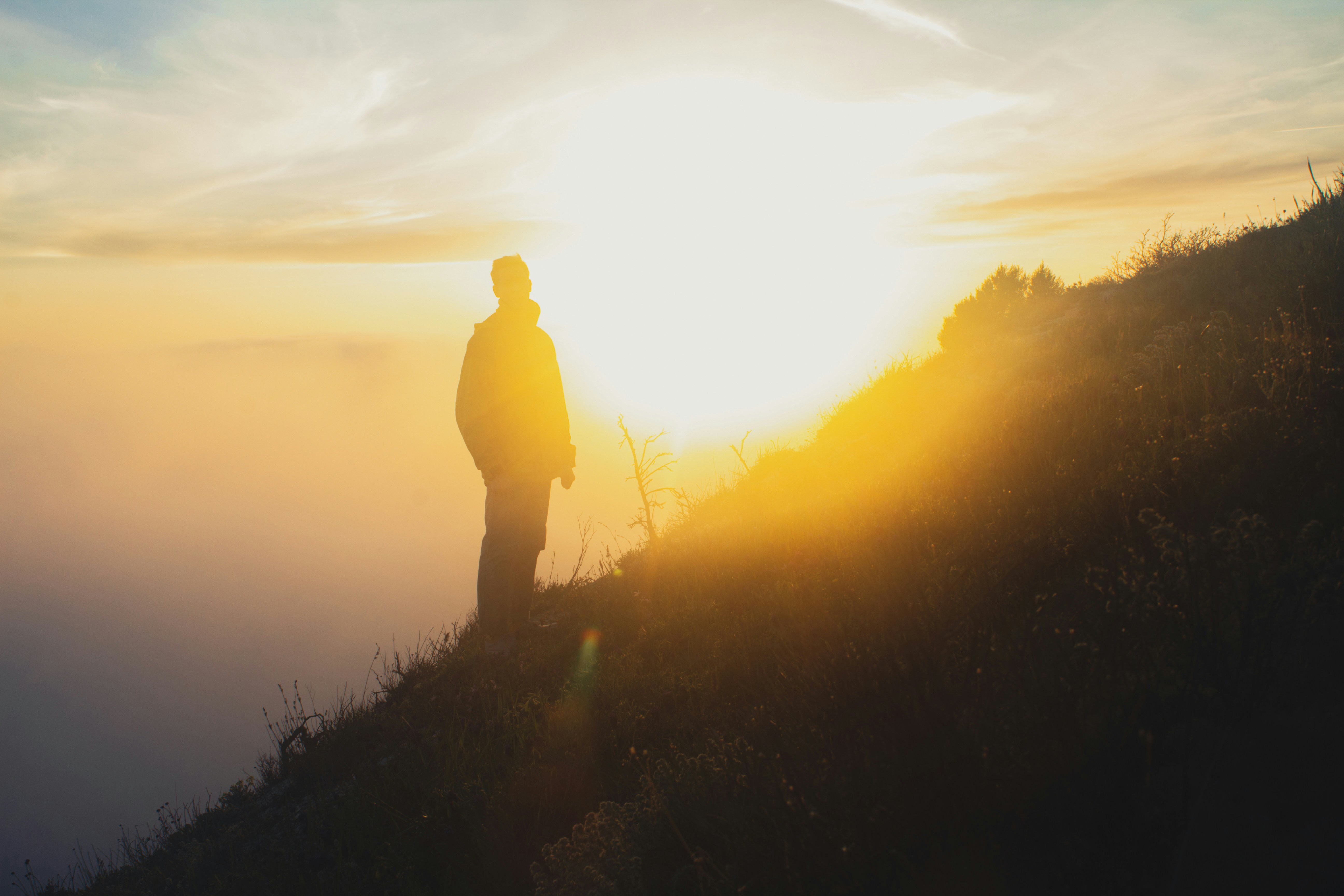 Traveler man is walking on hills among clouds. Beautiful Sunset on High mountains. Human inside Nature on blue sky background.