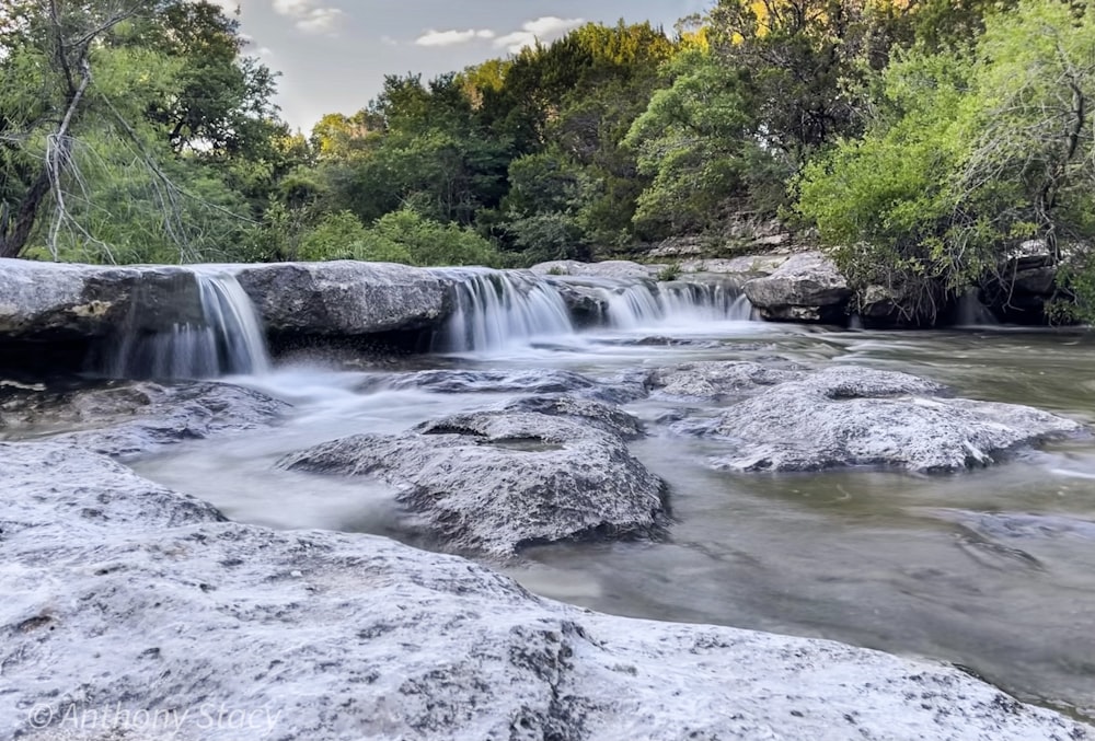 water falls in the middle of green trees during daytime