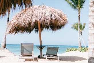 brown beach umbrella near white lounge chair under blue sky during daytime