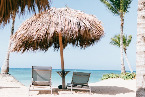 brown beach umbrella near white lounge chair under blue sky during daytime