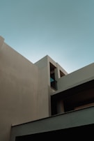 A minimalist architectural structure featuring clean lines and angular shapes, predominantly in shades of concrete gray and complemented by a clear blue sky.