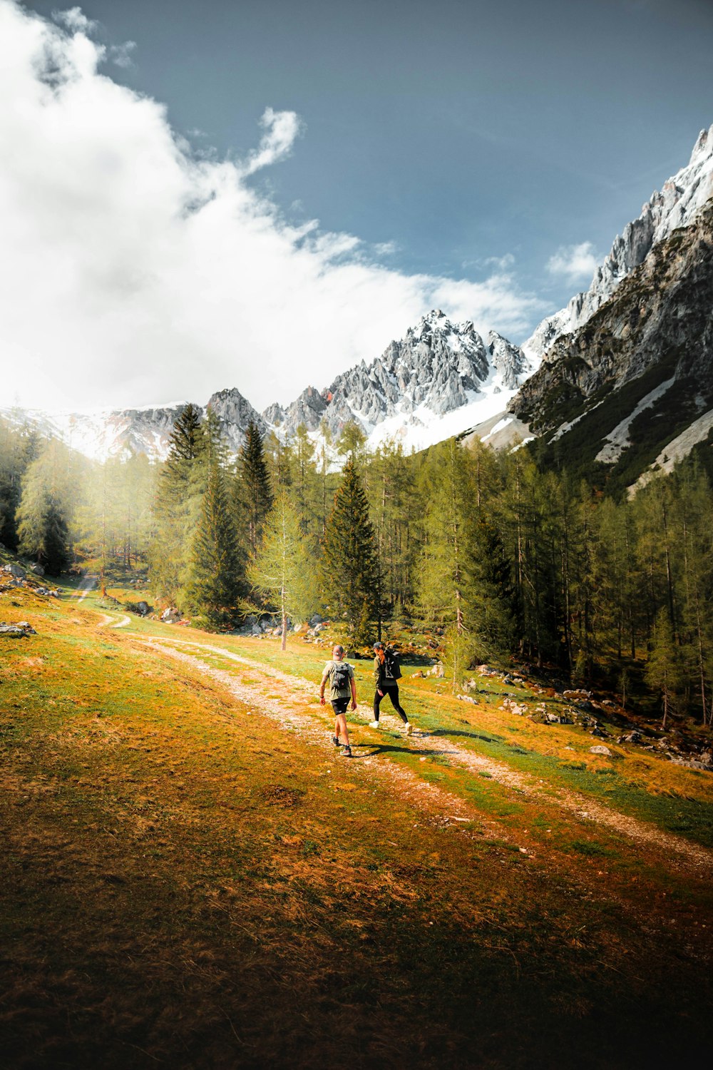 2 Personen fahren tagsüber auf einem Feldweg in der Nähe von grünen Bäumen und schneebedeckten Bergen