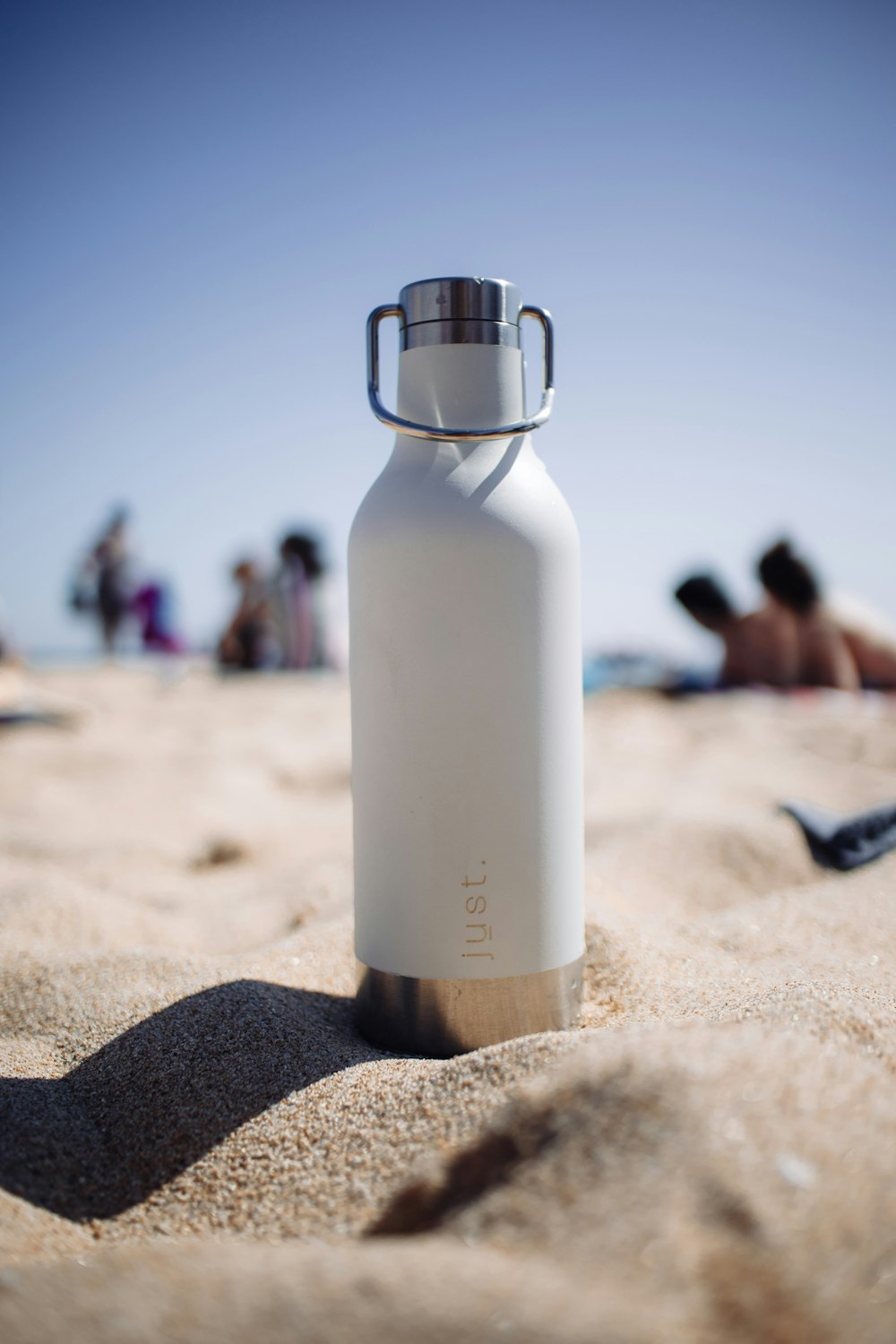 white and silver bottle on brown sand during daytime