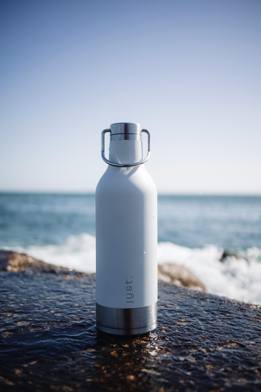 white and gray bottle on black rock near sea during daytime