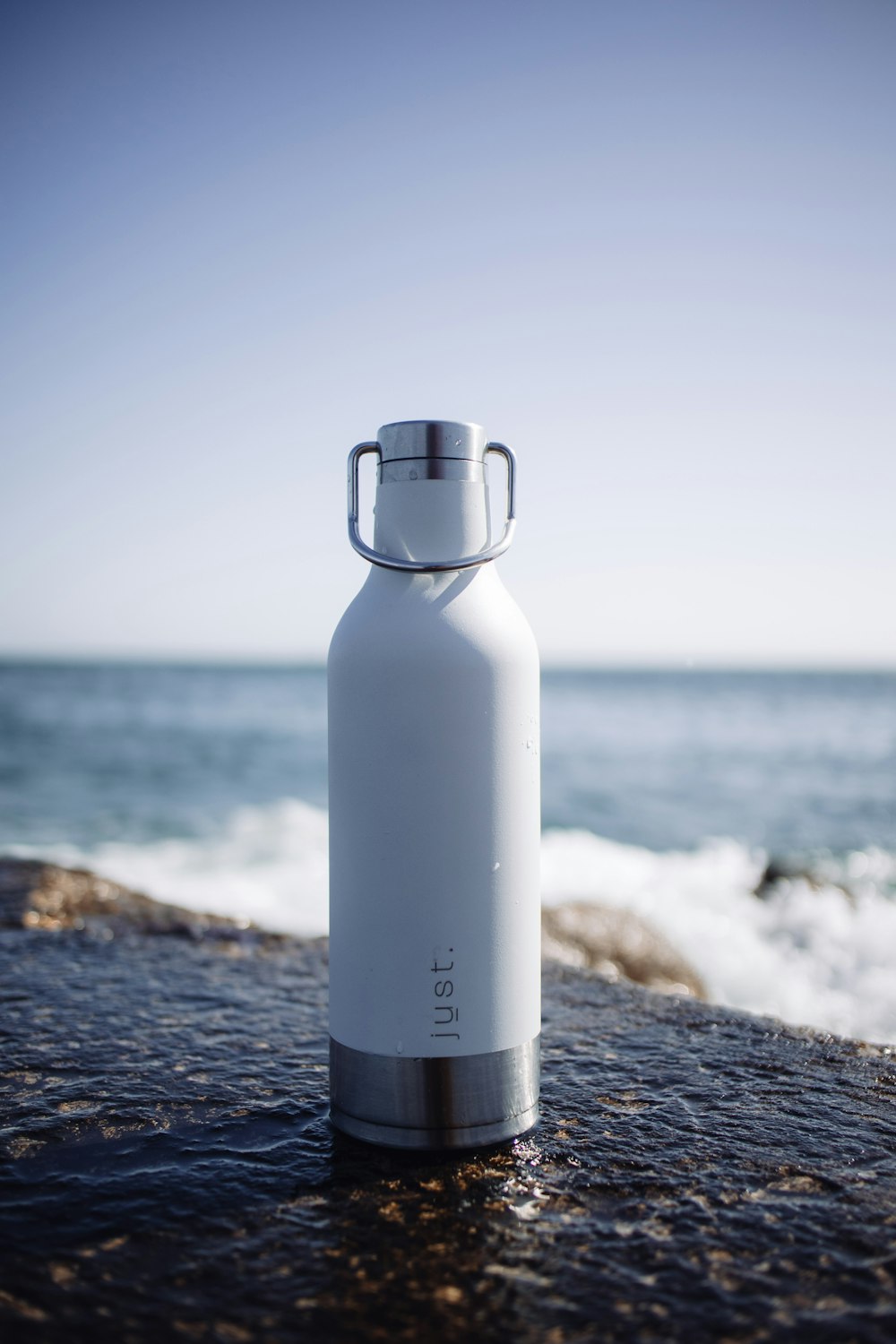 white and gray bottle on black rock near sea during daytime