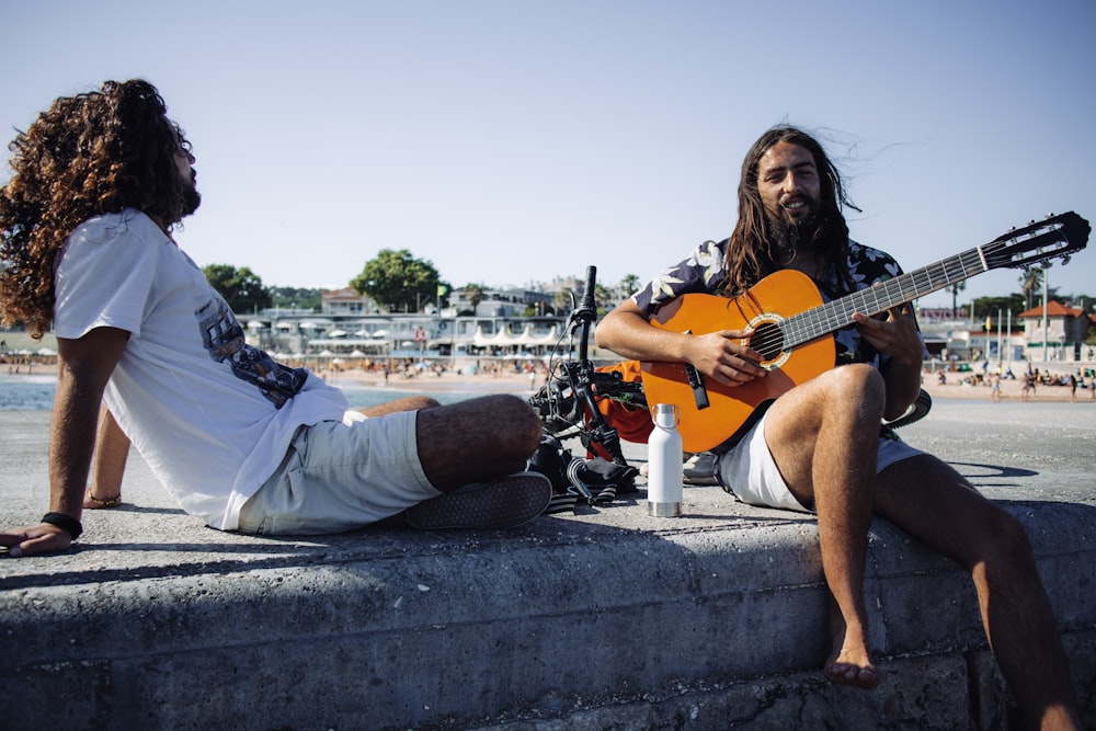 Hombre con camisa blanca tocando la guitarra acústica sentado en un banco de hormigón durante el día