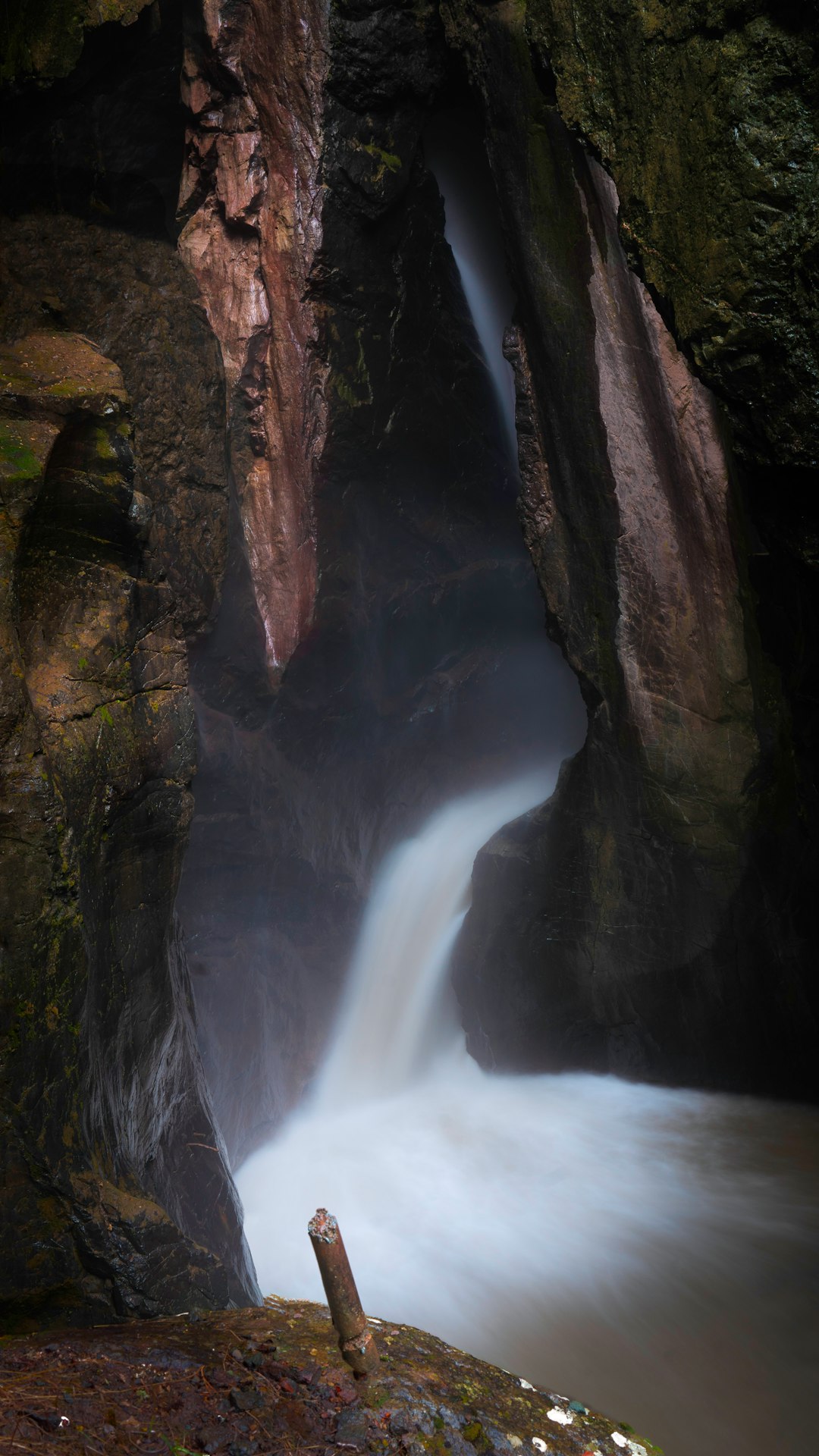 water falls between brown and green rock formation during daytime