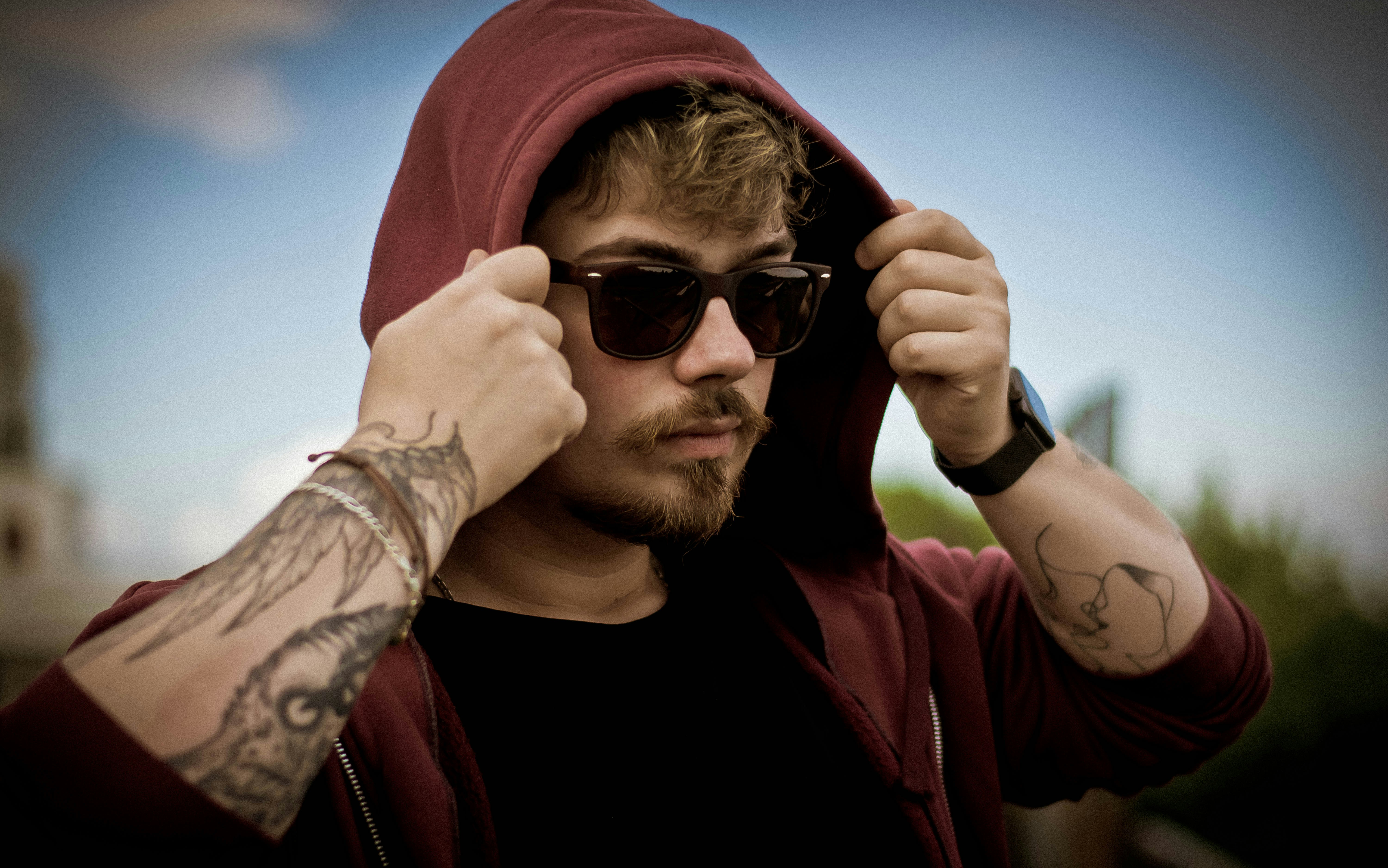 Mann im schwarzen Rundhalshemd mit schwarzer Sonnenbrille und rotem Kapuzenpullover