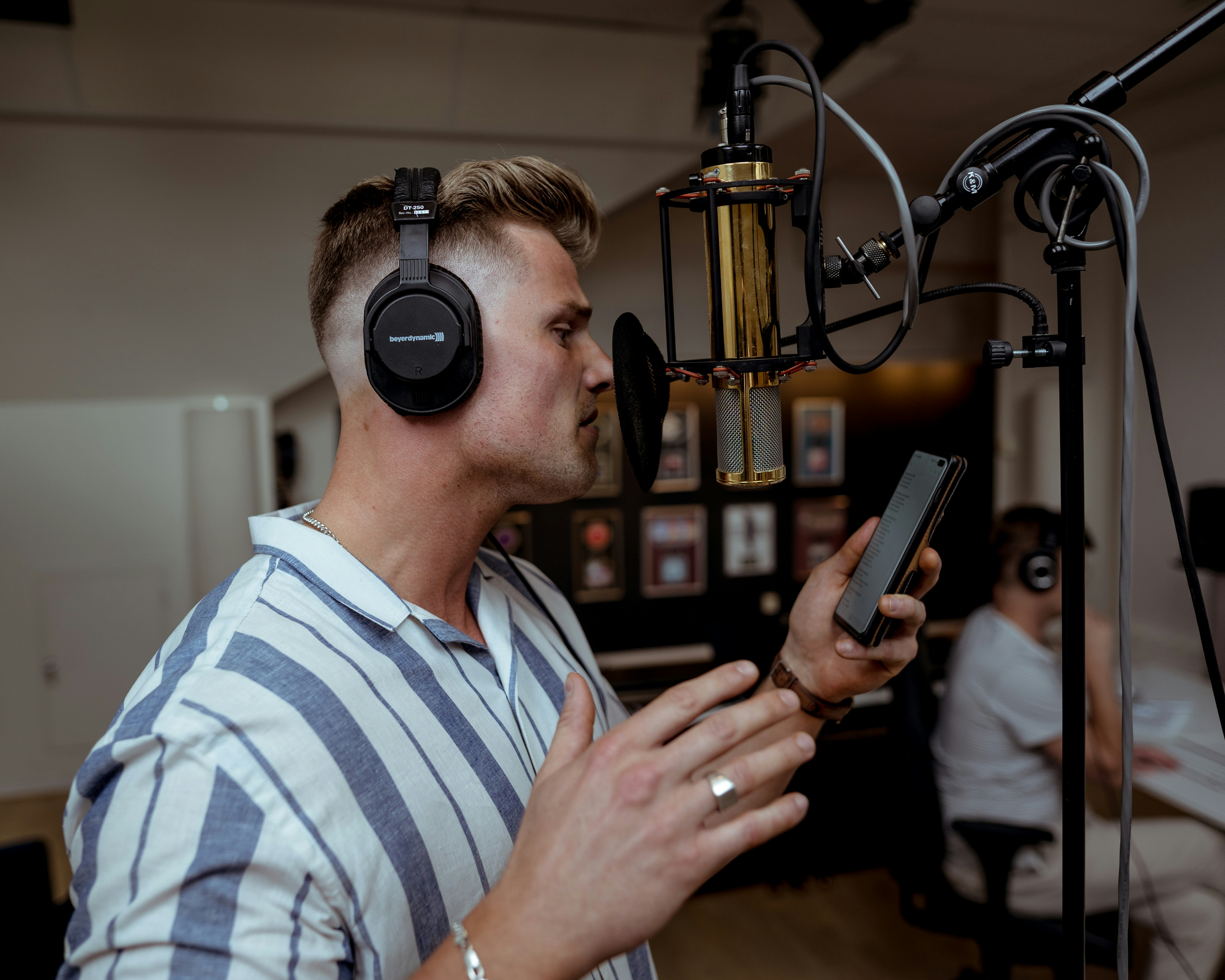 A man practices how to do voice overs into a studio mic, while an editor waits to add voice over to video projects.