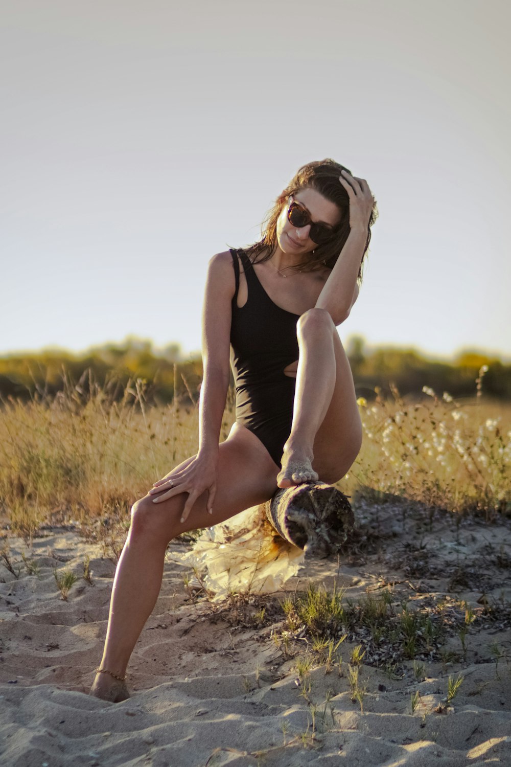 woman in black tank top and brown skirt sitting on brown grass field during daytime