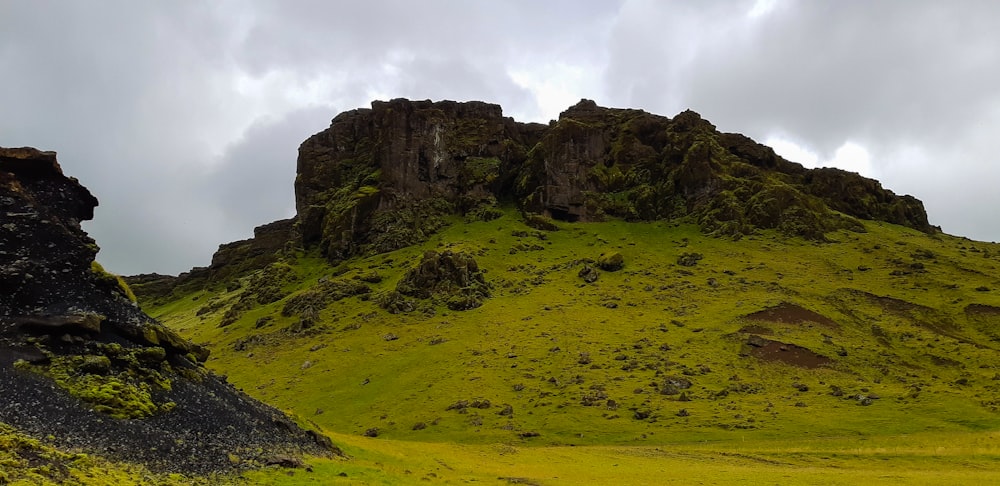 green grass field near brown rock formation under white clouds during daytime