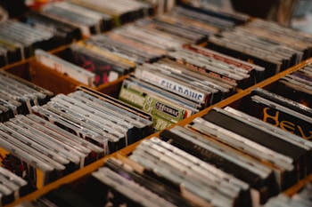 A collection of vinyl records organized in wooden crates, displayed at an angle. The spines of the records are visible, showcasing a variety of album covers and colors.