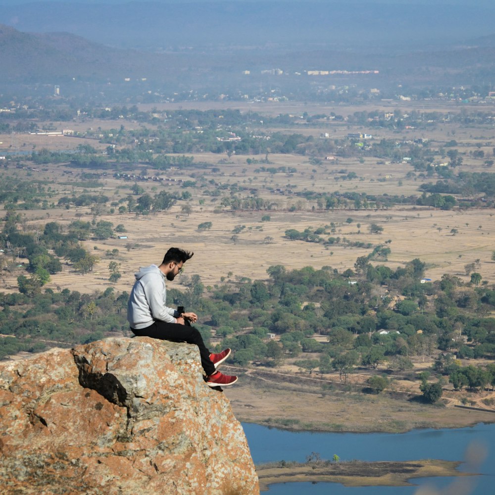 man in grey shirt sitting on rock formation during daytime