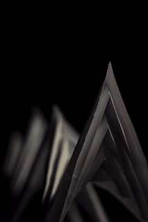 Angular paper shapes are arranged against a stark black background, creating a sharp contrast. The geometric forms are highlighted by soft lighting that accentuates their edges and folds.